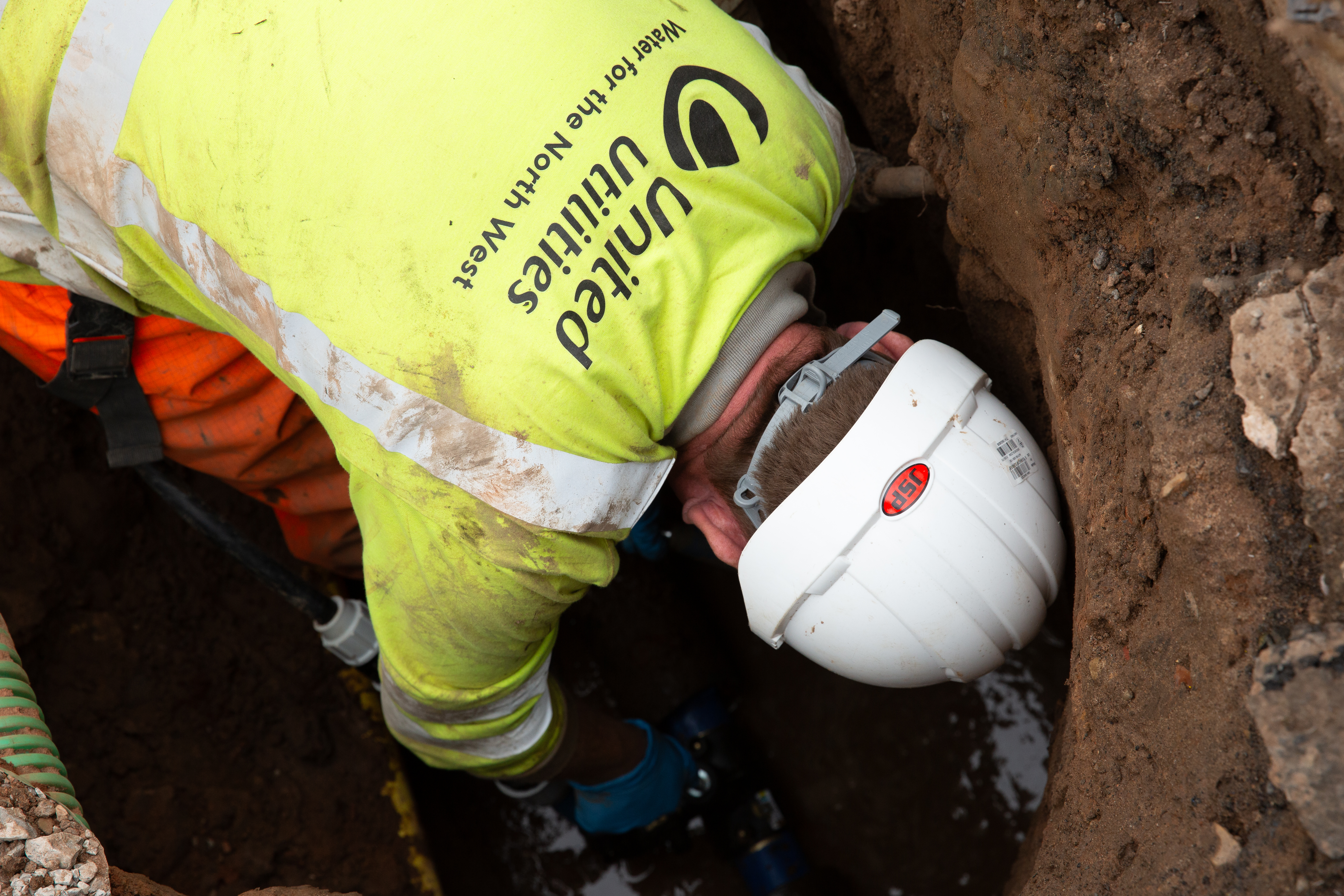 Worker crouched in ditch working on exposed pipe
